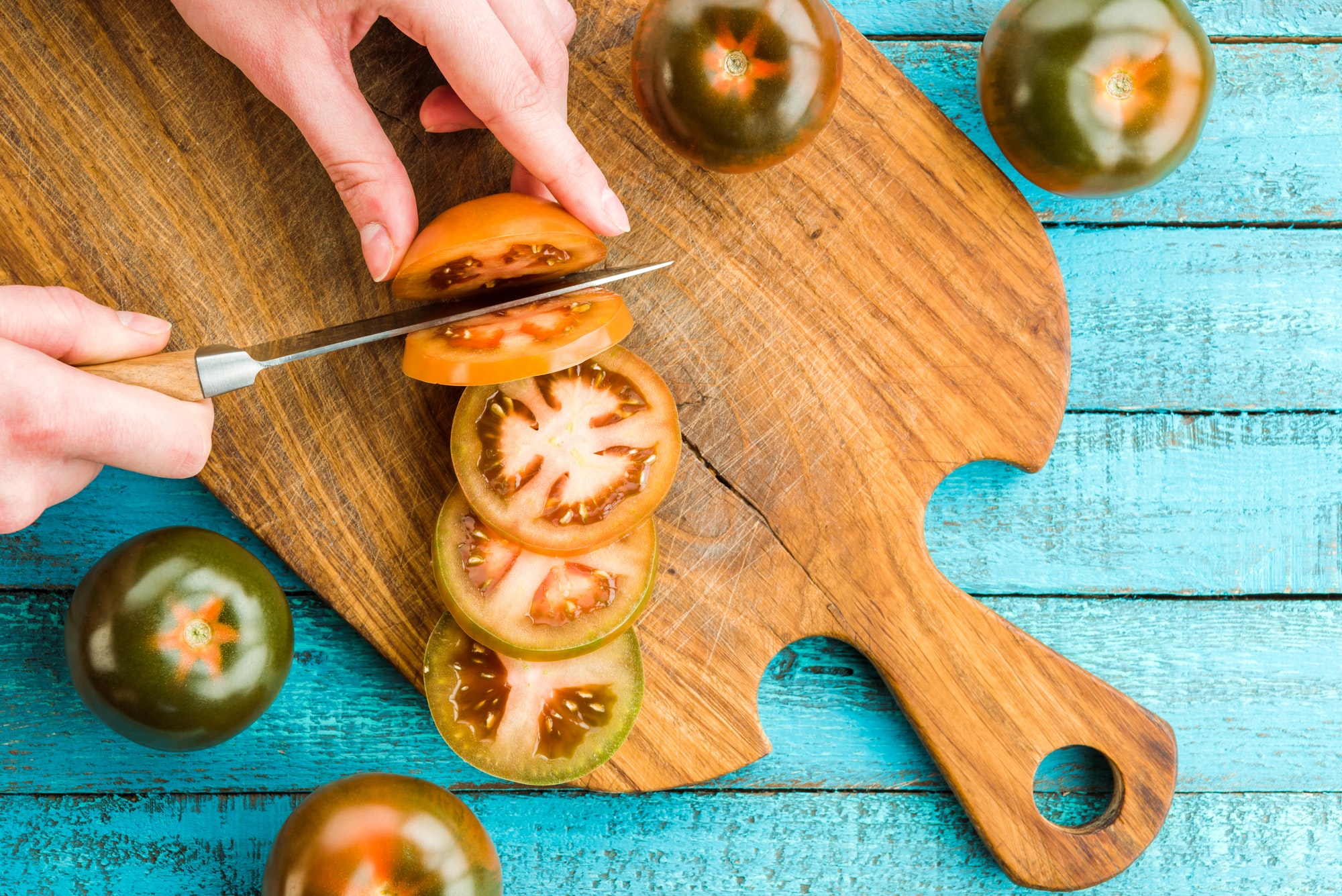 top view of hands cutting fresh tomatoes on cutting board